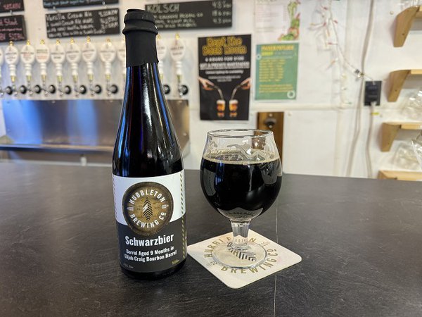 A bottle and a small glass of dark beer is on a slate gray counter.