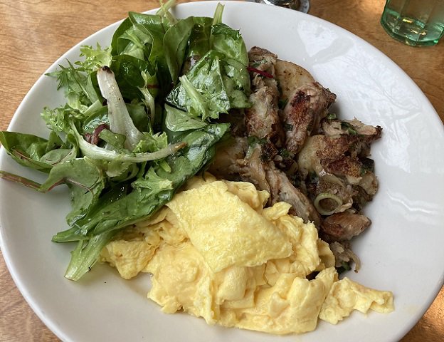 Greens, duck confit hash and scrambled eggs on a white plate.