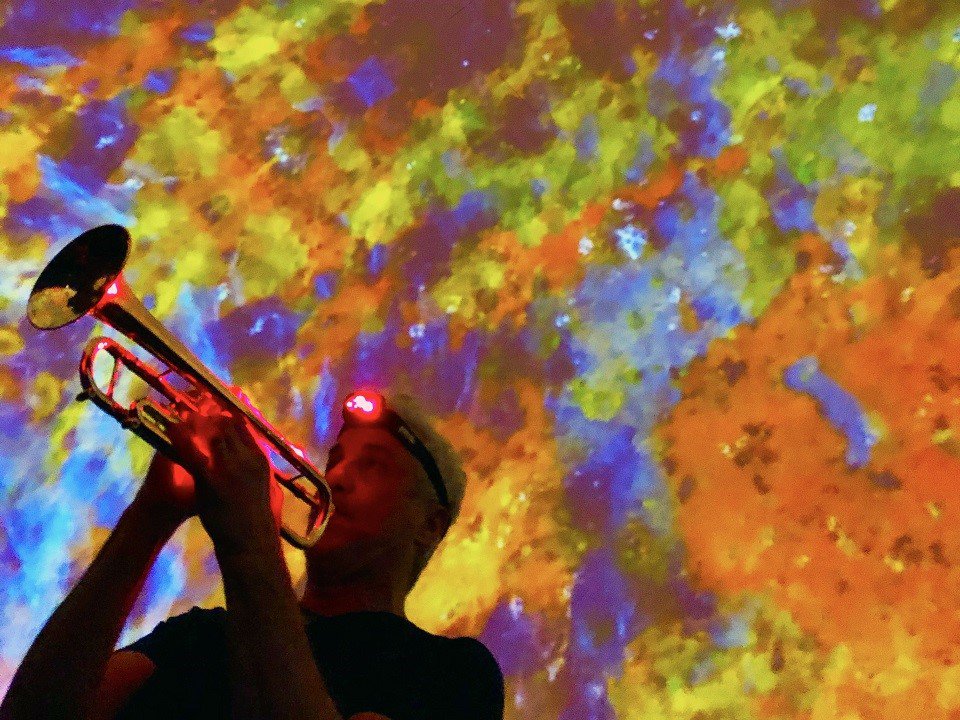 A person playing trumpet in front of a colorful projection.