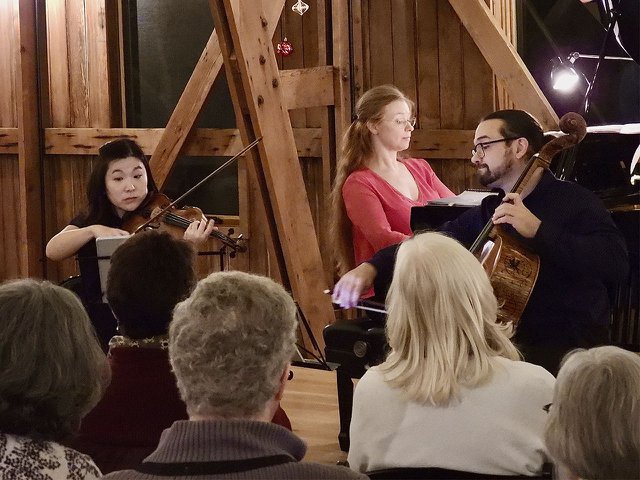 Three people playing chamber music in a well lit barn.
