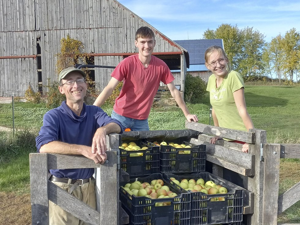 Chris McGuire and two children with milk crates full of apples with a barn in the background.