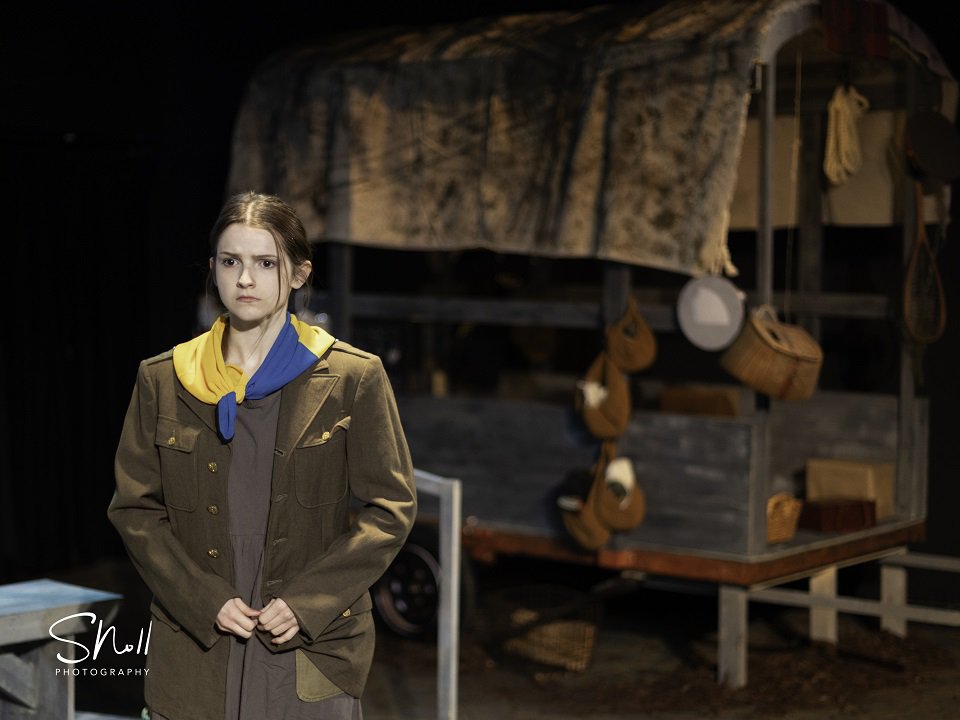 Abigail Hindle as Kattrin stands on stage looking forlorn with bleak backdrop.