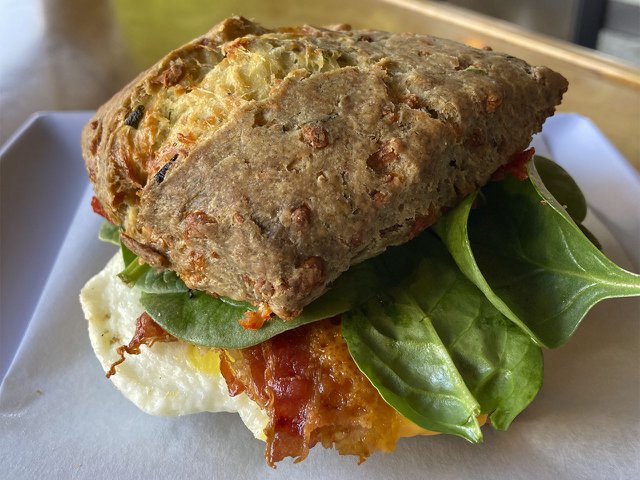 The brownish, squarish scone has some spinach greens, and egg and a bit of bacon peeking out from beneath it.