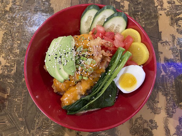 Red bowl filled with cukes, hard boiled egg, daikon, greens and shrimp tempura.