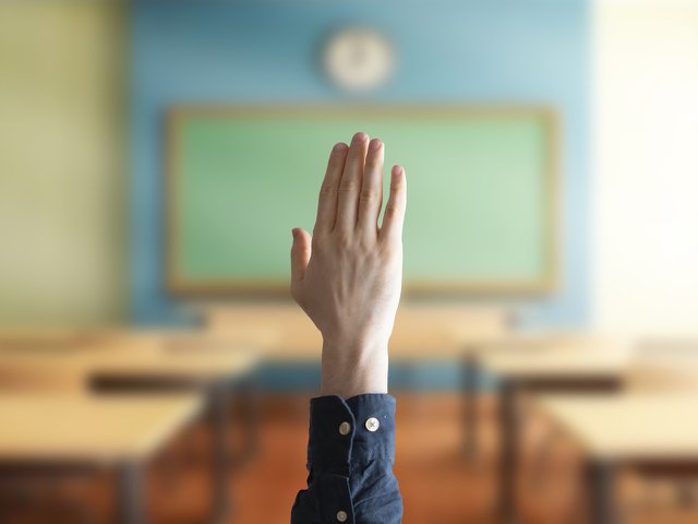 A hand raised to ask a question in a classroom setting.