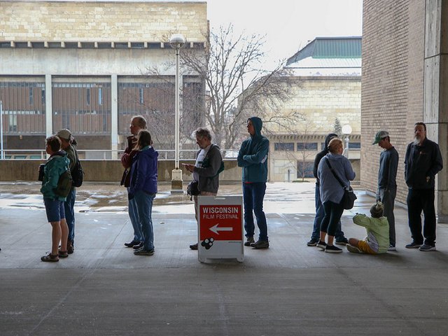A line of film fest attendees waiting to get into a Cinematheque showing with the Humanities building in the background.