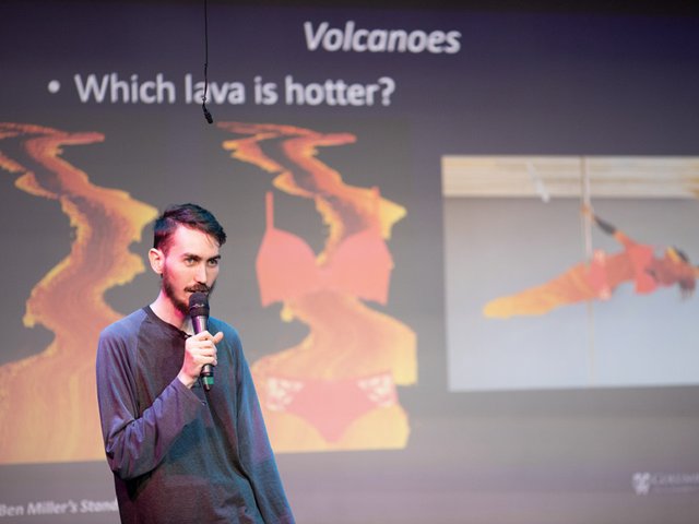 A man on stage with a microphone in front of a slide showing lava coming from a volcano.