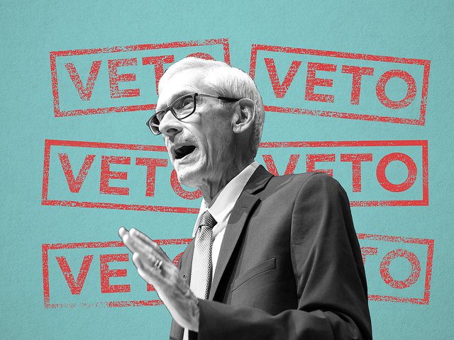 Tony Evers in front of several "veto" stamps.