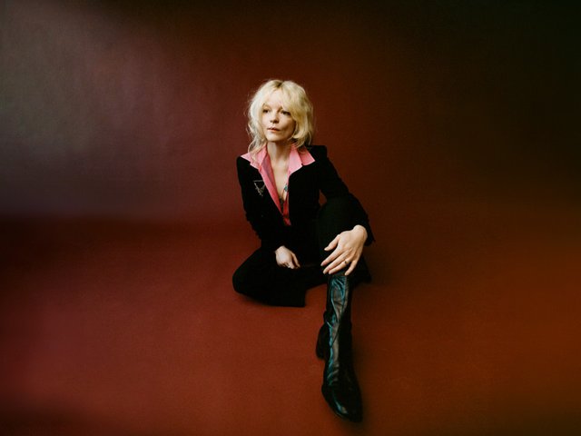 Jessica Pratt sitting in a photo studio in front of a red background.