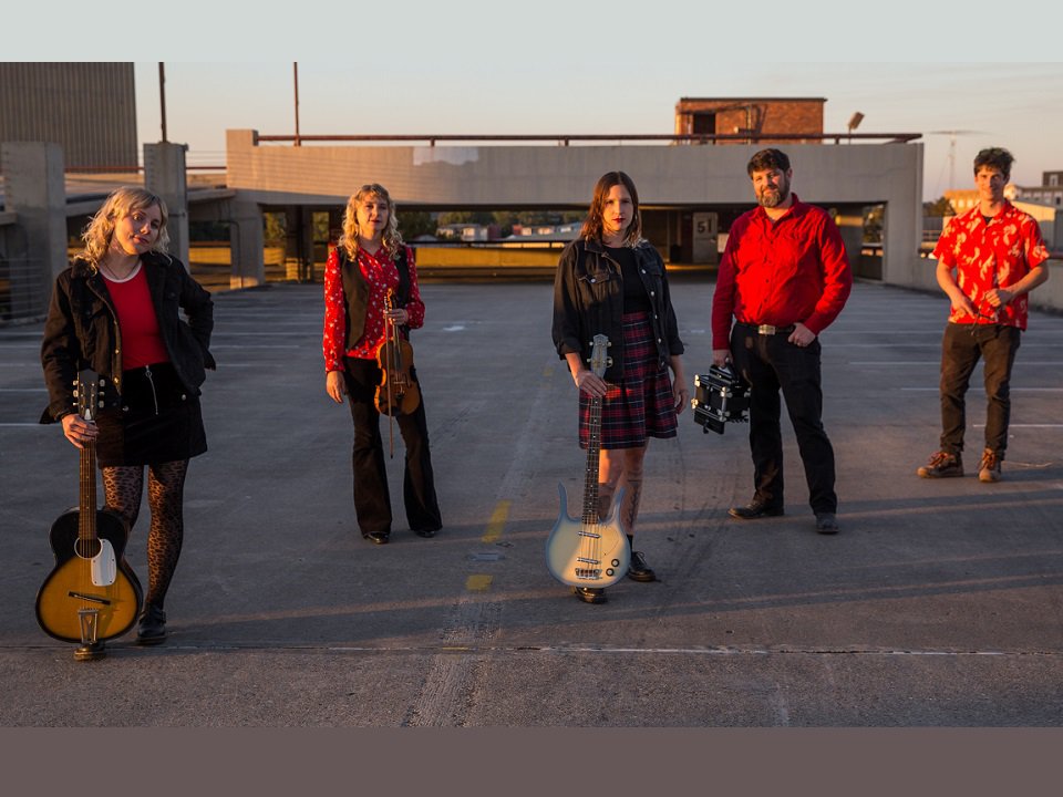 The band Daiquiri Queens and instruments standing in a parking lot.