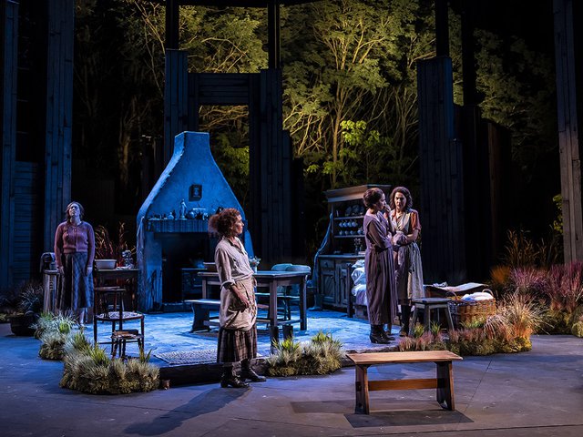 A moonlit stage set of an Irish home with a hearth and real trees lit in the rear