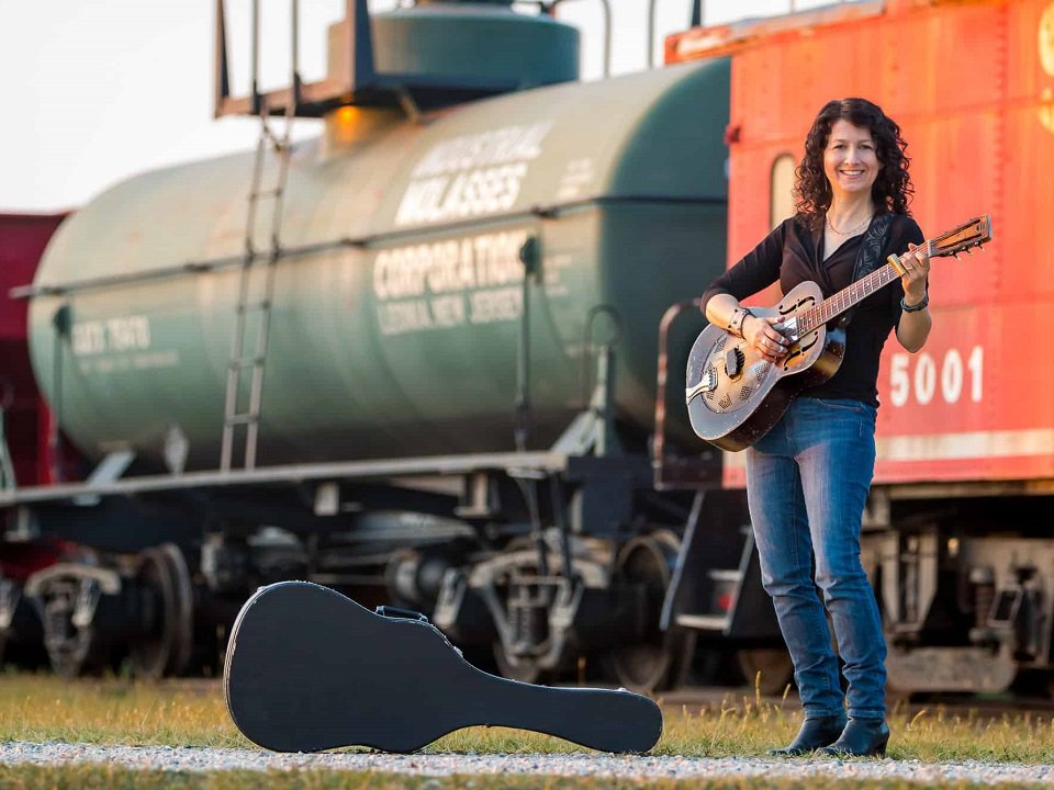 Donna Herula and guitar in front of a train.