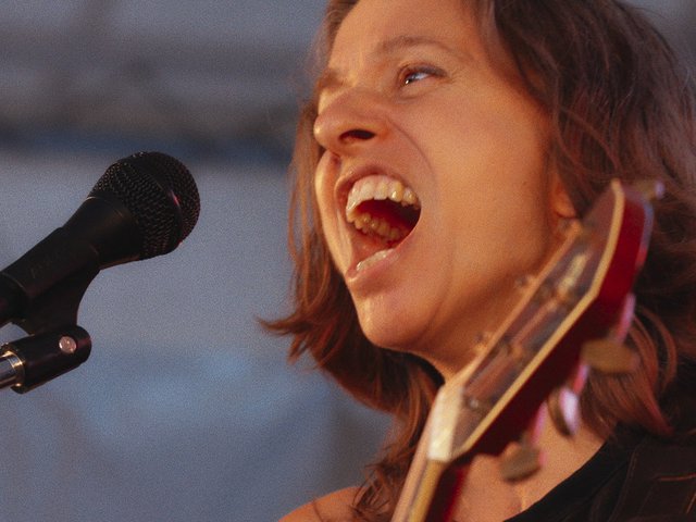 A close-up of Ani DiFranco singing into a mic.