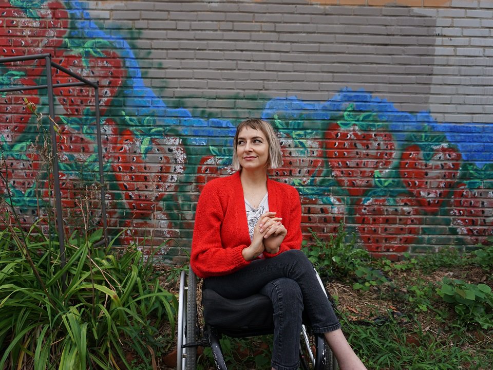 Rebekah Taussig in a wheelchair in front of a mural of strawberries.