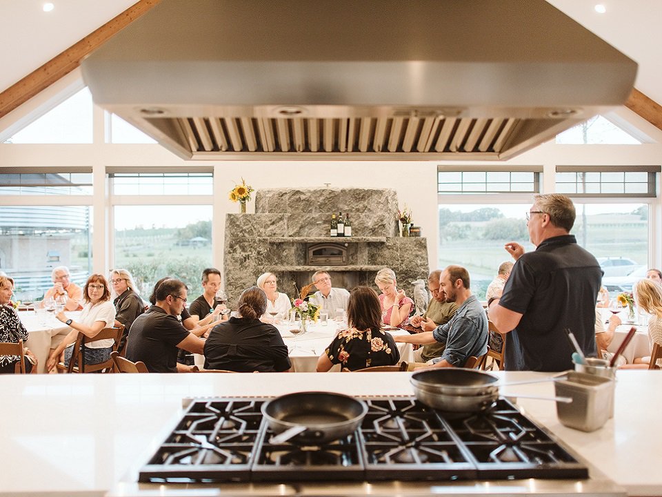 A group of people around a large table with a stove in the foreground.