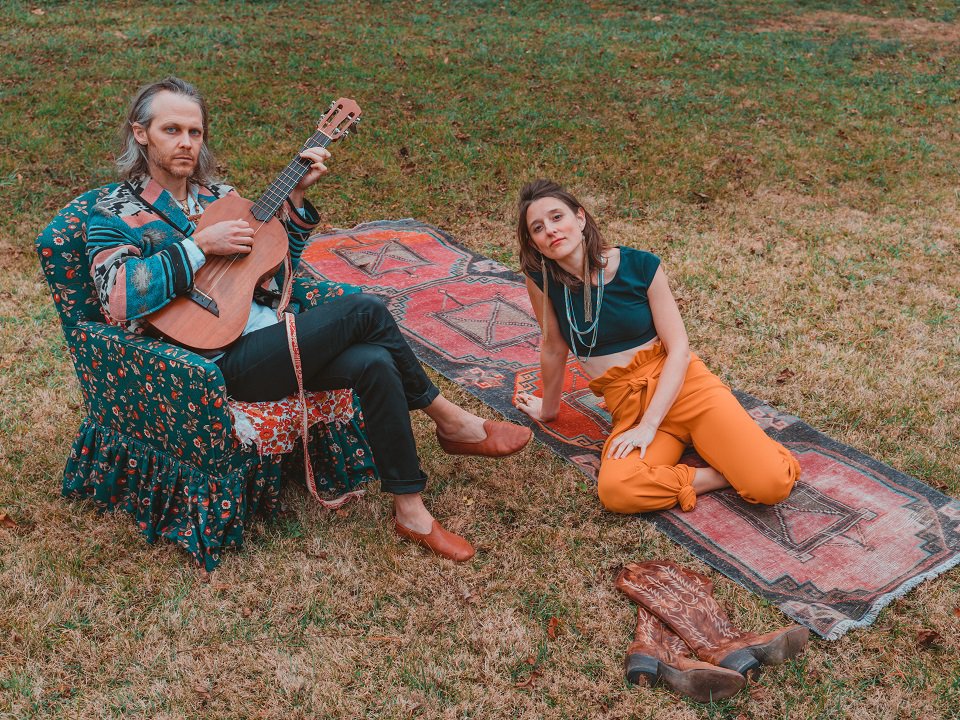 David Wax Museum members in a chair and on a blanket on the ground.