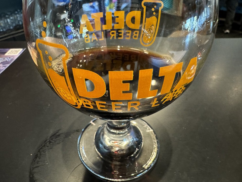 A Delta Beer Lab snifter glass with a dark beer in it.