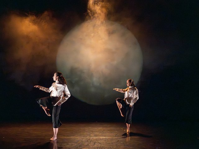 Two dancers in the same pose in front of a large moon in the UW Dance Department's Faculty Concert.