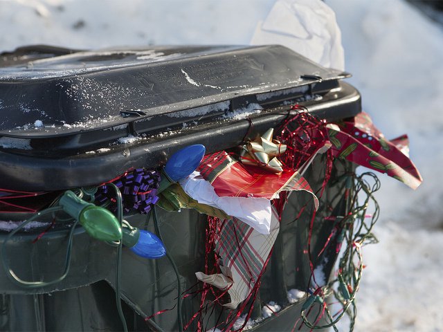 Christmas wrapping paper and bows spilling out of a full trash can.